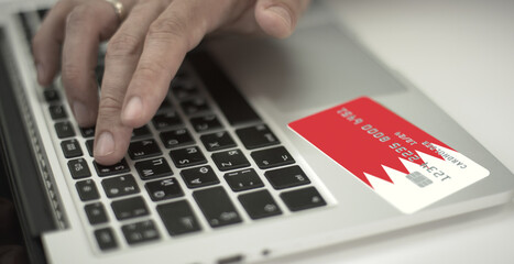 Man pays online with plastic bank card with printed flag of Bahrain. Fictional numbers