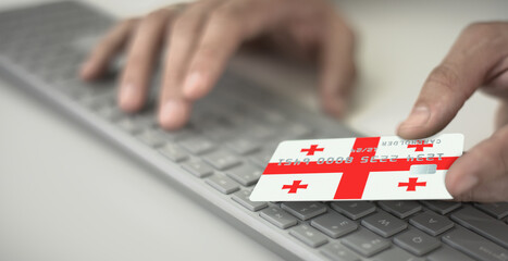 Man pays online with plastic bank card with printed flag of Georgia. Fictional numbers
