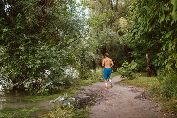 Fototapeta na wymiar Handsome fitness caucasian man in shorts trains and runs in the forest. Fitness in nature
