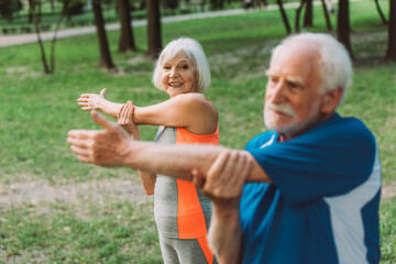 Fototapeta premium Selective focus of smiling senior woman exercising with husband in park