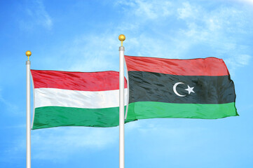 Hungary and Libya two flags on flagpoles and blue cloudy sky