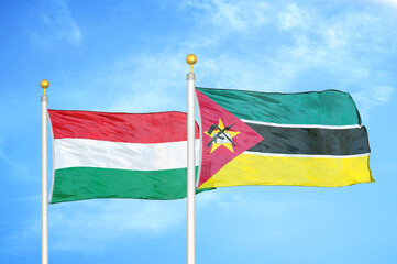 Hungary and Mozambique two flags on flagpoles and blue cloudy sky