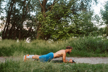 Sport fitness caucasian man with bare-chested in shorts trains and exercises in the forest. Push-ups in nature