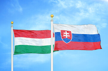 Hungary and Slovakia two flags on flagpoles and blue cloudy sky