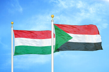 Hungary and Sudan two flags on flagpoles and blue cloudy sky
