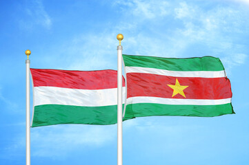 Fototapeta na wymiar Hungary and Suriname two flags on flagpoles and blue cloudy sky