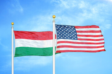 Hungary and United States two flags on flagpoles and blue cloudy sky