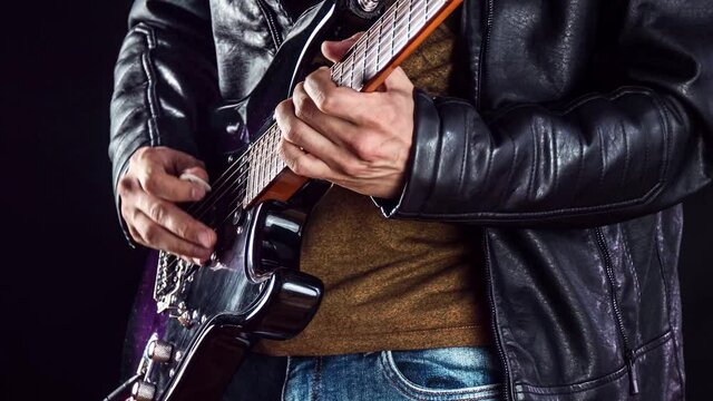 Guitarist plays solo on electric guitar. Rock performer plays melody on instrument. Man in a leather jacket plays jazz.