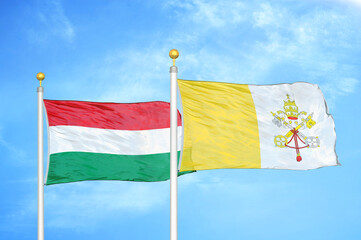 Hungary and Vatican two flags on flagpoles and blue cloudy sky