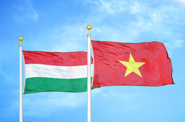 Hungary and Vietnam two flags on flagpoles and blue cloudy sky