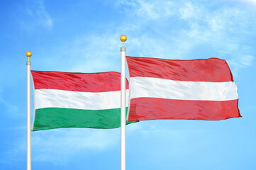 Hungary and Austria  two flags on flagpoles and blue cloudy sky