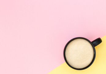 Coffee with foam on a light pink and yellow background with copy space