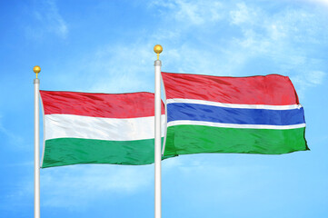 Hungary and Gambia two flags on flagpoles and blue cloudy sky