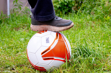 Boy legs with white and orange ball instead of soccer ball standing on the grass. Father's day, outdoors activity, sport family weekend.