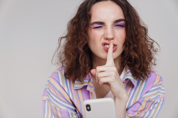 Image of ginger woman showing silence sign while using smartphone