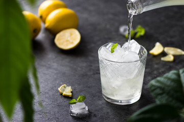 a translucent drink from a bottle is poured into a glass containing ice cubes. Summer refreshing drink is poured into a glass with ice