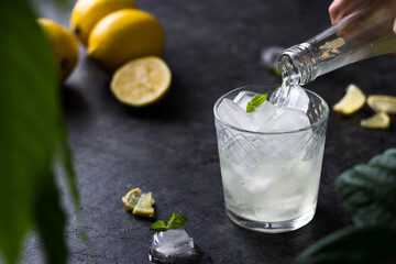 a translucent drink from a bottle is poured into a glass containing ice cubes. Summer refreshing drink is poured into a glass with ice