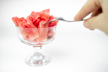 take a chopped watermelon pieces with fork from the glass cup, summer fruit refreshment