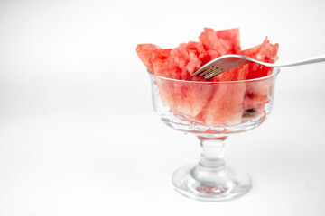 take a chopped watermelon pieces with fork from the glass cup, summer fruit refreshment