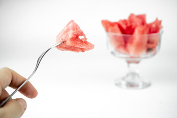 take a chopped watermelon pieces with fork from the glass cup, summer fruit refreshment