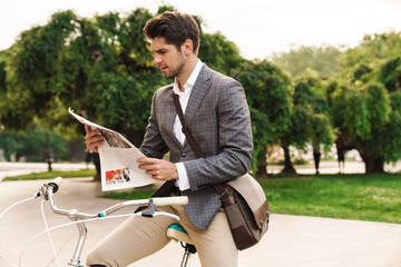 Business man outdoors reading newspaper on a bicycle