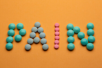 Word pain on orange background written with colorful pills. Painkiller tablets taken by prescription.