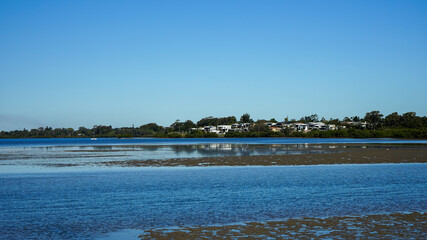 View across the bay at low tide, with homes on the shore reflected in the shallow water. Redland Bay, Queensland, Australia.