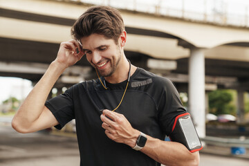 Image of athletic smiling sportsman using earphones while working out