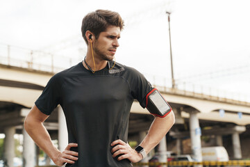 Image of displeased young sportsman using earphones while working out