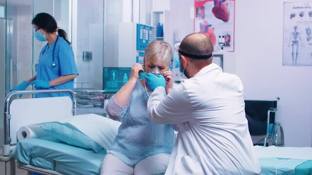 Doctor putting an oxygen mask on old retired senior woman during COVID-19 coronavirus outbreak in modern private hospital or clinic. Fighting infection and disease medicine and quarantine