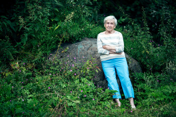 Elderly woman stands in the Park among the green trees.