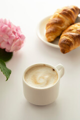 Croissant and a cup of coffee with pink hydrangea on background. Breakfast concept.