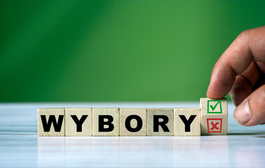 The hand turns the wooden cube and changes the polish word WYBORY (english = elections) with green positive tick check box and red reject X check box. - obrazy, fototapety, plakaty