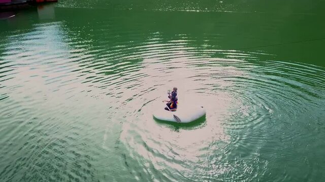 Aerial view of two kids in inflatable boat having fun near the tropical coastline in Kenyir Lake, Malaysia. Low altitude.