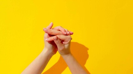 Top view of the hands of a woman who is rubbing her hands on a yellow background
