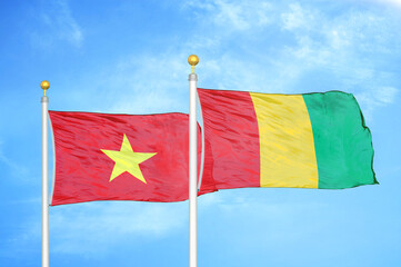 Vietnam and Guinea two flags on flagpoles and blue sky