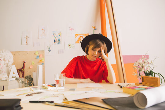 Sad girl Illustrator artist clutched head sitting at table in studio. State of apathy, frustration and creative crisis