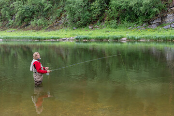 Fototapeta na wymiar Elderly fisherman in water threw fishing rod. Fly fishing in mountain river.
