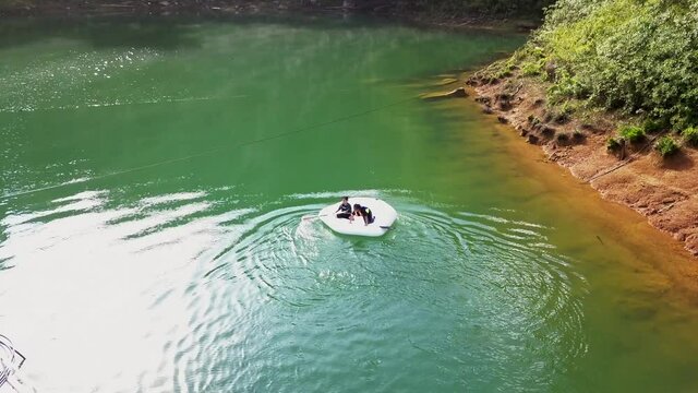 Low altitude aerial view of two kids rotating in inflatable boat having fun near the tropical coastline in Kenyir Lake, Malaysia.