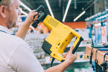 A man holds a puncher in his hands. Concept man selects a product in a hardware store.