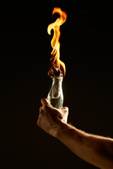 Male's hand with a burning Molotov cocktail isolated on black background. Concept photography about...