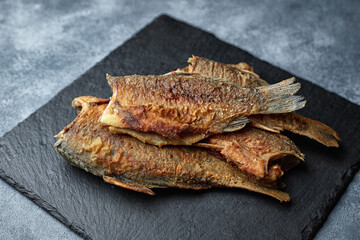 Fried fish crucian carp, on a black stone, on a gray background