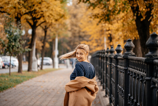 An attractive girl in a bezel-less polto walks in the autumn park. Style and fashion concept. Yellow trees. Autumn time.
