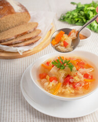 Cabbage soup in white bowl and spoon with soup in the hand, and also bread, parsley and spice on the table. 