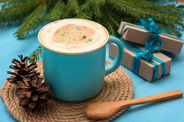 Freshly brewed coffee with an airy foam on a light blue wooden table. With gifts and fir needles.