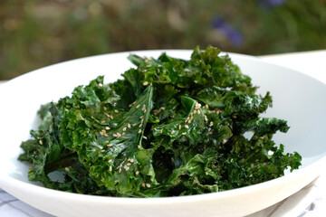 Crunchy baked curly kale chips with sesame seed on white plate. 