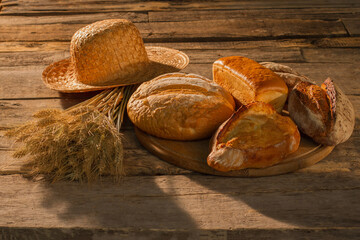 Rural still life on vintage wooden background. Various bread loaves, wheat ears and straw hat on rustic wooden boards.