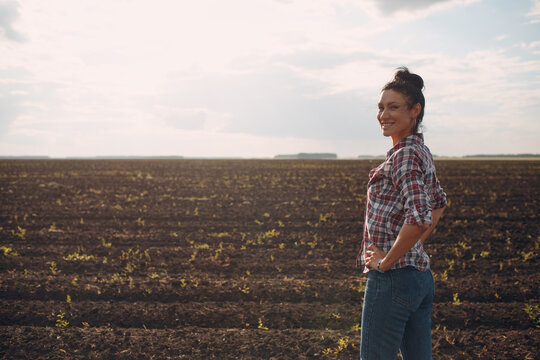 Woman farmer standing and looking agricultural field soil.