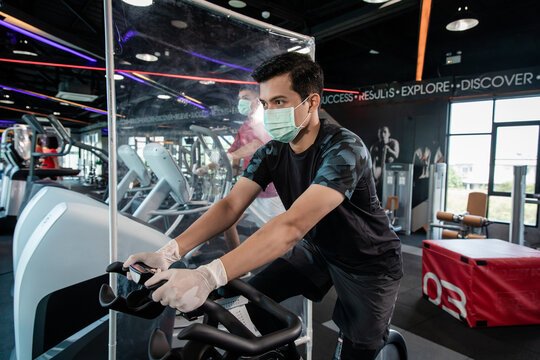 Young man running on a treadmill wearing surgical mask & latex rubber gloves, COVID-19 pandemic social distancing rules while working out in  a gym and have Acrylic Partition, new normal & social dist