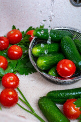 fresh juicy tomatoes cucumbers and parsley lie in the sink under the tap, hygiene and health washing vegetables